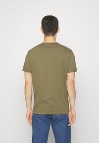 Tricou scurt cu maneci, de culoare verde olives, din bumbac, cu guler rotund și un design simplu, purtat cu blugi albaștri. Textură netedă, croială casual.