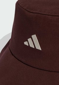 Bordeauxfarbene Mütze aus strukturiertem Stoff, die auf der Vorderseite ein auffälliges, weiß gesticktes Logo mit drei Streifen zeigt.