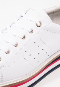 Baskets en cuir blanc avec ferrures dorées, bout rond, accents perforés et semelle extérieure multicolore avec des bandes rouges et bleues marine.
