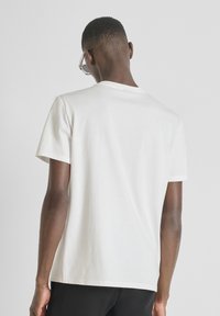 Camiseta blanca de manga corta con cuello redondo, hecha de algodón suave, con una textura lisa y un diseño simple.