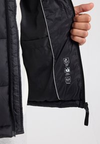 Black padded jacket interior with a smooth finish, featuring a side pocket and printed icons for windproof, water-repellent, and padded qualities.