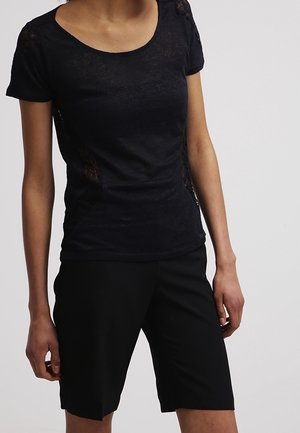 T-shirt noir à manches courtes avec un col arrondi et des accents en dentelle sur les côtés, assorti à un short noir longueur genou.