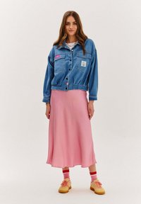 Džínová bunda s dvoma prednými vreckami, ružovou nášivkou a elastickým pásom, skombinovaná s dlhou ružovou saténovou sukňou a žltými teniskami.