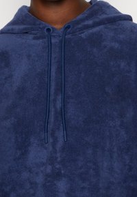 Granatowa bluzka z kapturem wykonana z miękkiego, szczotkowanego materiału. Posiada sznurek ze plastikowymi końcówkami oraz luźny krój.