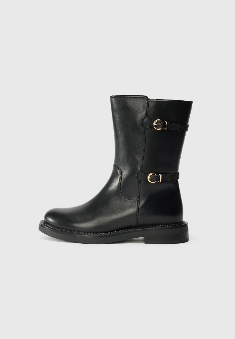 Botte en cuir noire mi-mollet à bout arrondi, talon bas et deux sangles à boucle dorée sur le côté sur un fond uni.