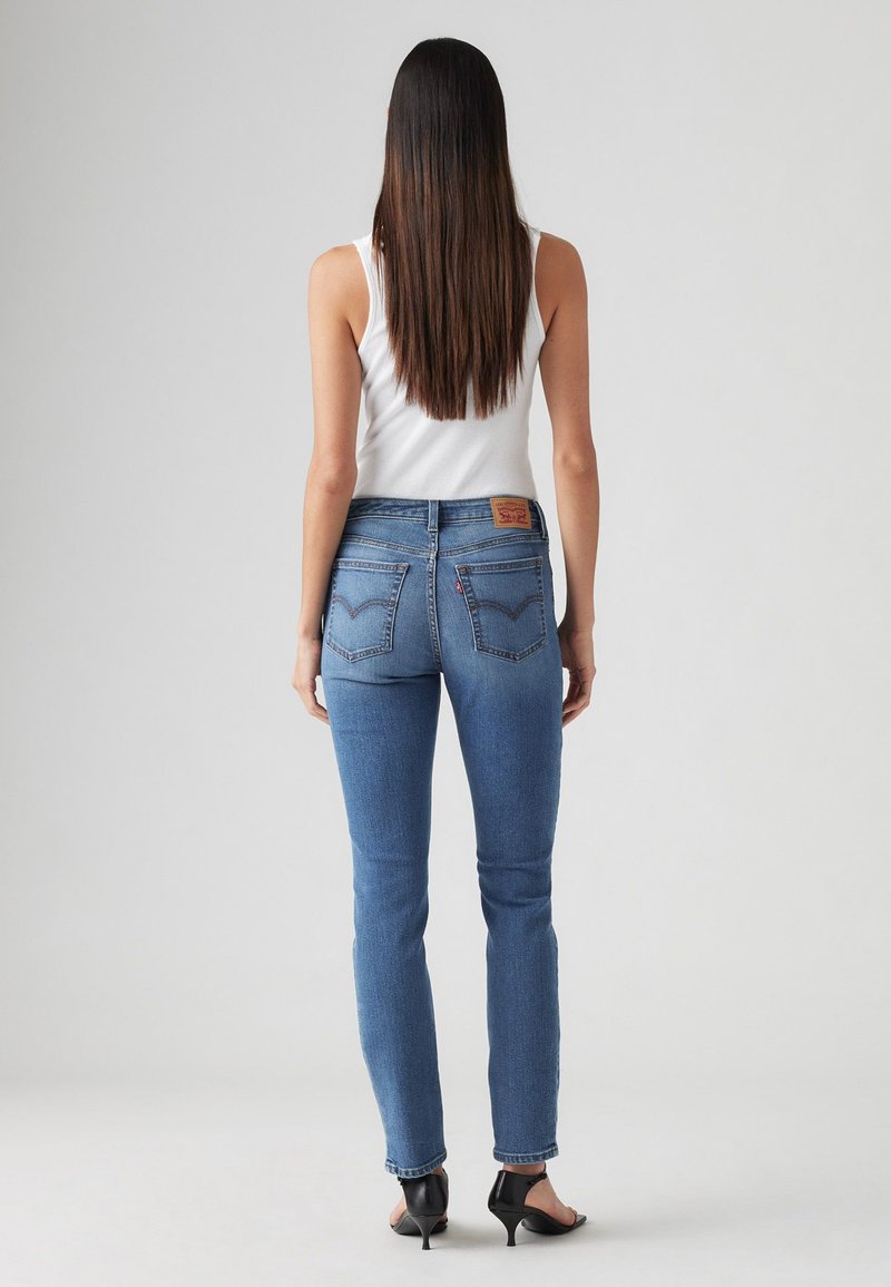 Jeans de mezclilla azul de tiro alto con un corte slim. Detalles de costura notables en los bolsillos y una etiqueta de cuero de marca en la parte posterior de la cintura.