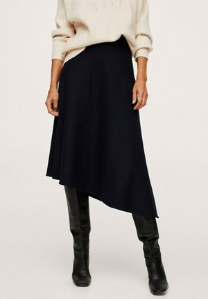 Falda de punto negra asimétrica con textura suave, presenta una cintura ajustada y una silueta fluida, combinada con botas negras hasta la rodilla.