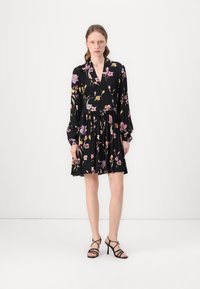 Abito nero a fiori con maniche lunghe, scollatura a V e vita arricciata, caratterizzato da fiori viola e gialli. Abbinato a tacchi neri con cinturini.