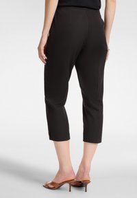 Pantaloni cropped neri con una texture liscia e design fitted. Indossati con sandali con tacco marroni, caratterizzati da un dettaglio della fascia minimalista.