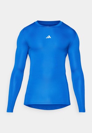 Plava dugorukava atletska majica s prilagođenim dizajnom, glatkom teksturom, okruglim izrezom i bijelim Adidas logom na gornjem lijevom dijelu prsnog koša.