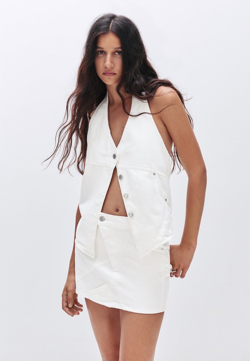 Witte mouwloze top met een V-halsontwerp en knoopsluiting, gecombineerd met een bijpassende A-lijn rok met gestructureerde naden en minimalistische details.