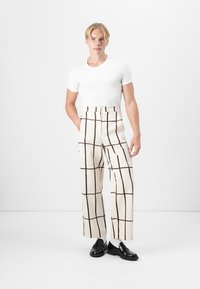 Camicia bianca aderente e pantaloni a gamba larga color crema con un motivo a griglia marrone. Tessuto liscio e design a vita alta, abbinati a scarpe nere.
