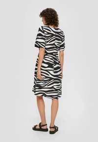 Schwarz-weißes Zebra-Muster-Kleid mit kurzen Ärmeln, runder Halslinie und lockerer Passform, das bis zur Mitte des Oberschenkels reicht. Der Stoff wirkt weich und strukturiert.