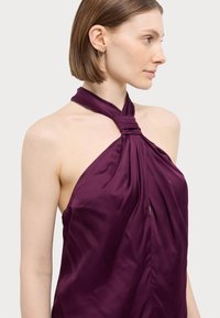 Top halter viola con tessuto arricciato e dettaglio a nodo sul collo; texture di satin morbido; presenta un leggero taglio sotto il busto.