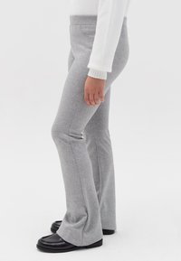 Grijze flare-pantalons gemaakt van rekbare stof, met een gladde afwerking, platte tailleband en een subtiele glans. Gemaakt in combinatie met zwarte loafers.