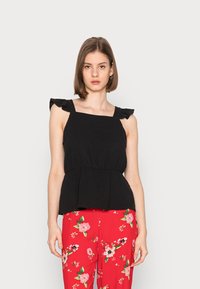 Top peplum preto com alças franzidas, tecido texturizado e corpete ajustado, combinado com calças vibrantes com estampado floral vermelho.