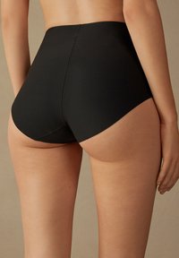 Sous-vêtements noirs taille haute avec une texture lisse, présentant un design simple et des coutures plates, mettant en valeur un ajustement près des hanches.