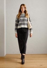 Knitted sweater with black and white geometric patterns, high-waisted black denim skirt, and black ankle boots. Beige bag slung over shoulder.