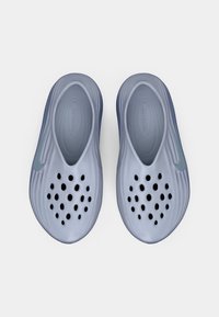 Pár modrých nazúvacích topánok s viacerými ventilačnými otvormi na vrchu a logom Nike swosh na každej strane, pohľad zhora.