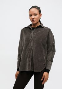 Pelēka kordurojas krekls ar apkakli, pogu aizdari priekšpusē un garām piedurknēm. Raksturo relaxed fit siluets un fakturēta virsma.