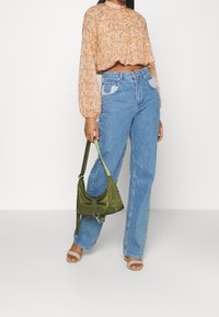 Blusa floral naranja recortada con detalles de botones, jeans de tiro alto azul claro, bolsa de satén verde y sandalias de punta abierta beige.