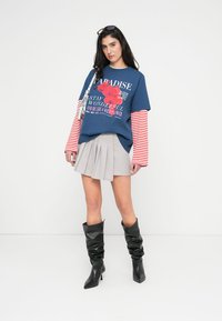 Μπλε κοντομάνικο μπλουζάκι με σχέδιο ροζ λουλουδιών, κόκκινα και λευκά ριγέ μανίκια, γκρι πλισέ φούστα και μαύρα μπότες με τακούνι έως το γόνατο.