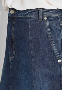 Jeans in denim di colore blu scuro, con cuciture gialle, design a cinque tasche e chiusura frontale con bottone. Tessuto morbido e aderente.