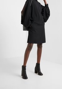 Musta pitkähihainen paita, jossa on volyymikkaat hartiat, yhdistetty mustan minihameen ja nilkkakenkien kanssa. Struktuuriltaan musta-valkoinen pilkullinen käsilaukku.