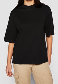 Černé tričko s krátkým rukávem vyrobené z měkké bavlny, s vysokým výstřihem a volným střihem, s lemovanými rukávy a přímým střihem.