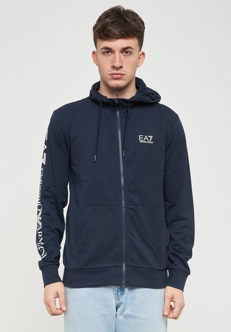 Felpa con zip navy realizzata in tessuto liscio, con un fit rilassato, cappuccio regolabile con cordoncino e dettaglio del logo sul petto e sulla manica.