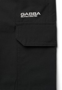 Juodas audinys su lygiu tekstūra, su pataisomu kišeniu ir baltu siuvinėtu logotipu "GABBA" bei tekstu "RELATABLE SINCE 1983."
