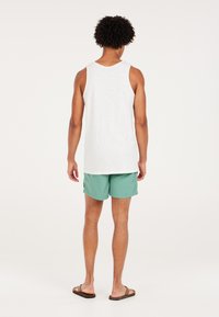 Witte tanktop voor heren met ronde hals, gedragen met mintgroene zwembroek. Sandalen aan de voeten. De nadruk ligt op casual zomerkleding.