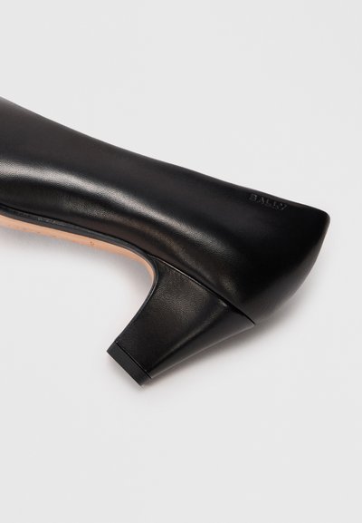 Chaussure à talon haut en cuir noir avec un bout pointu et un talon carré. Présente une texture lisse et un logo de la marque en relief sur le côté.