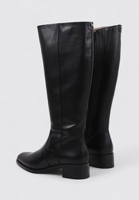 Bottes noires en cuir montantes jusqu'aux genoux avec un bout carré et un talon bas empilé. Présentent une texture lisse et des détails subtils de coutures.