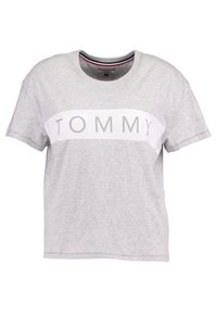Grå t-shirt med kort ärm i bomull, med ett vitt horisontellt band med texten "TOMMY" i ljusgrått över bröstet.
