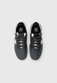Para czarnych, białych i szarych sneakersów Just Cavalli Milano z sznurówkami, widzianych z góry na białym tle.