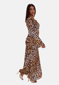 Robe maxi à imprimé léopard avec de longues manches évasées, présentant un mélange de teintes marron, noir et blanc dans un tissu lisse et fluide.