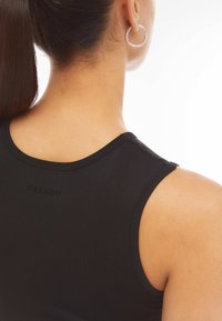 Top negro sin mangas con escote redondeado. Fabricado en tejido suave. Presenta un sutil logo "FREDDY" en la parte de atrás. Pelo recogido.