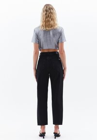 Camiseta gris cortada, jeans negros de tiro alto y pierna recta, textura suave, diseño de cinco bolsillos, combinados con tacones negros, visto desde la parte trasera.