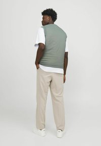 Lichtgrijze puffer vest over een wit t-shirt, beige broek en witte sneakers; heeft een gladde textuur en een casual pasvorm.