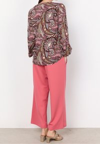 Blouse multicolore à motif cachemire avec des manches amples, associée à un pantalon rose ample et des sandales beige avec un design à brides tressées.