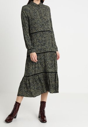 Vestido negro de manga larga con un patrón floral que presenta acentos en verde, amarillo y azul. Terminado con un dobladillo en capas y ribete negro.