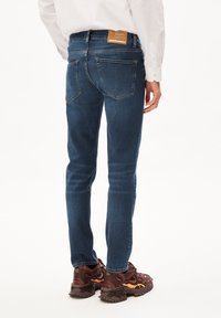 Jeans ajustados de denim en color azul con cintura media, detalles de costura, bolsillos traseros y una etiqueta de marca en la cinturilla.