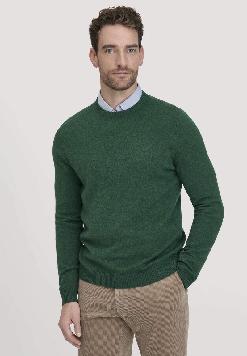 Grüner gestrickter Rundhalsausschnitt-Pullover aus weichem Stoff, kombiniert mit einem hellblauen Hemd mit Kragen. Auffällige gerippte Bündchen und Saum.