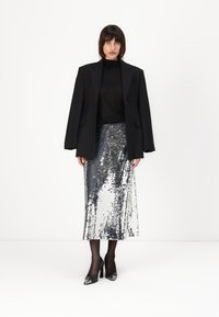 Black oversized blazer over a sheer black top, paired with a silver sequin midi skirt. Black heels and sheer tights complete the look.