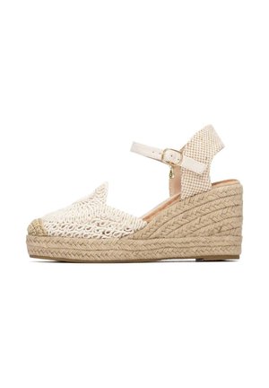 Sandalia de cuña tipo espadrille beige con suela de yute trenzado, puntera tejida y correa ajustable en el tobillo con hebilla dorada y charm.