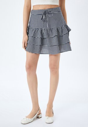 Jupe à motif vichy en bleu marine et blanc, dotée d'un design à volants, d'une taille à lien ajustable et d'une forme évasée. Fabriquée en tissu léger.