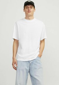 Hvid t-shirt med korte ærmer og rund halsudskæring, lavet af blød bomuld. Båret med lyseblå, afslappet pasform denim bukser. Sort cap på hovedet.