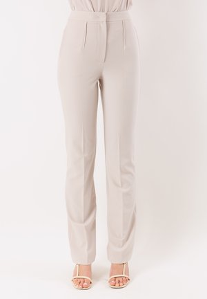 Pantaloni beige a vita alta, su misura, con pieghe frontali, abbinati a tacchi open-toe beige con cinturini.