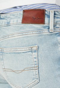 Lyseblå denimjeans med et lær patch med "Pepe Jeans London" logo, standard baklomme-design og kontrasterende sømdetaljer.